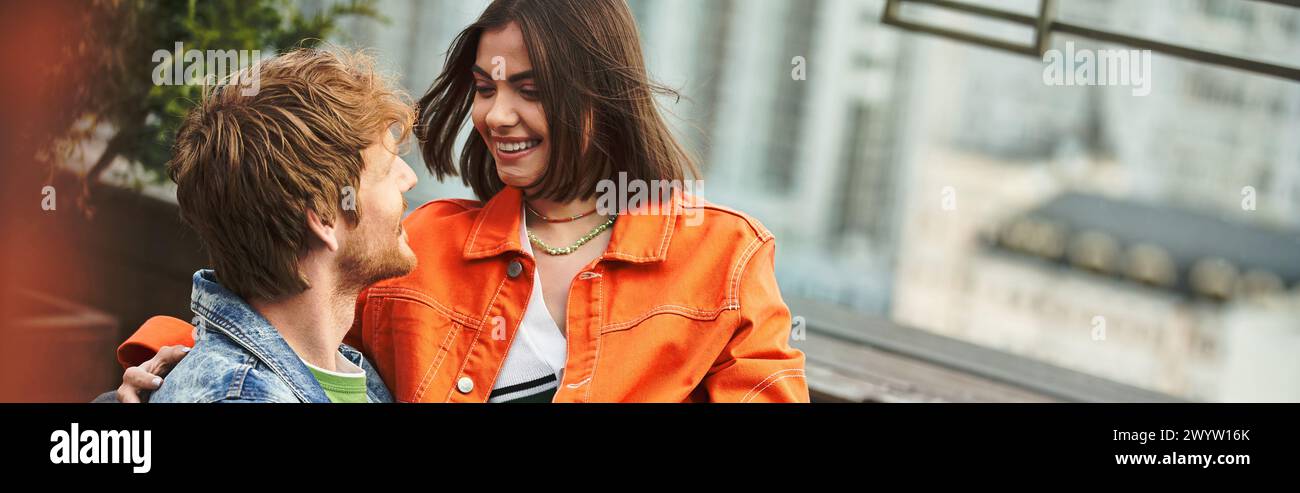 Ein stilvoller Mann und eine stilvolle Frau stehen Seite an Seite, beide tragen markante orange Jacken Stockfoto