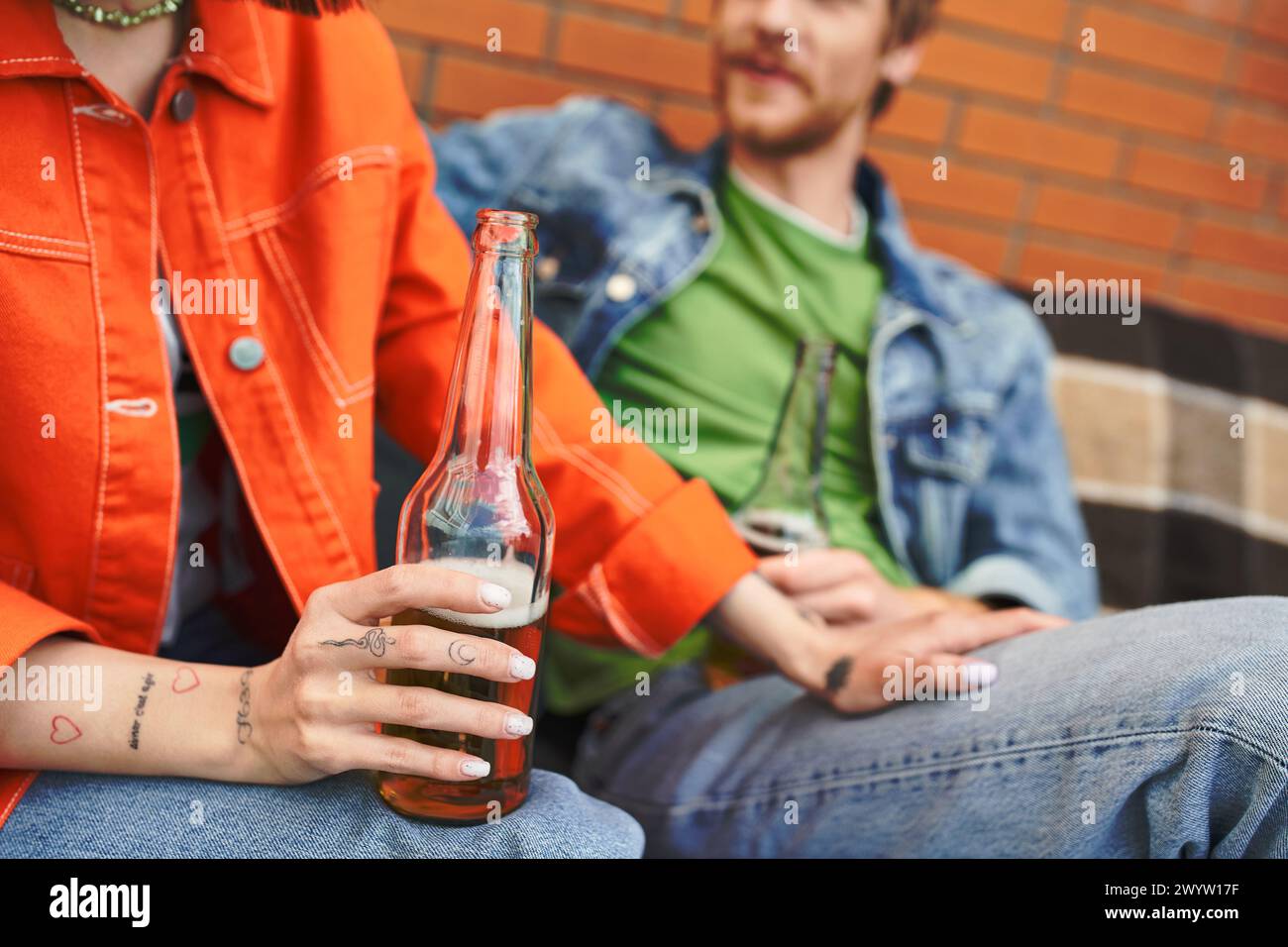 Ein Mann sitzt neben einer Frau, während sie eine Flasche Bier hält, und teilt einen Moment der Entspannung und Verbindung in einer gemütlichen Umgebung Stockfoto