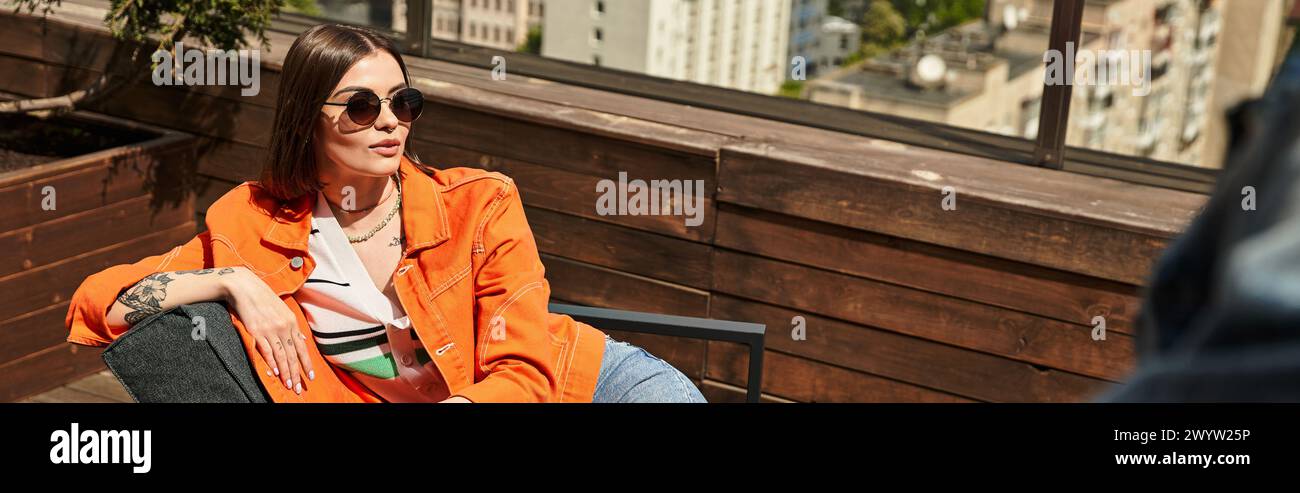 Eine Frau in einer orangen Jacke sitzt friedlich auf einer Holzbank und genießt einen Moment der Entspannung in einer ruhigen Umgebung im Freien Stockfoto