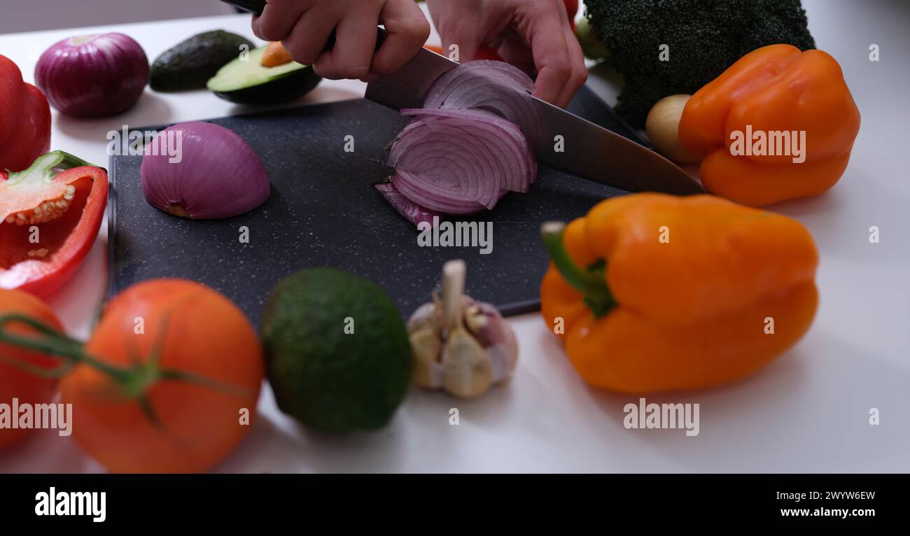 Koch schneidet rote Zwiebeln an Bord unter Gemüse aus der Nähe Stockfoto