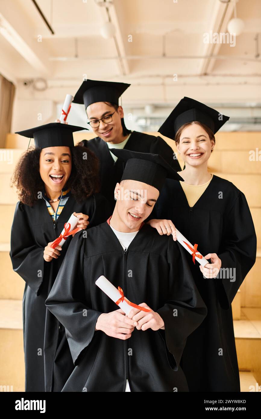Verschiedene Gruppen von Studenten in Abschlusskleidern und akademischen Mützen posieren glücklich für ein Foto drinnen. Stockfoto