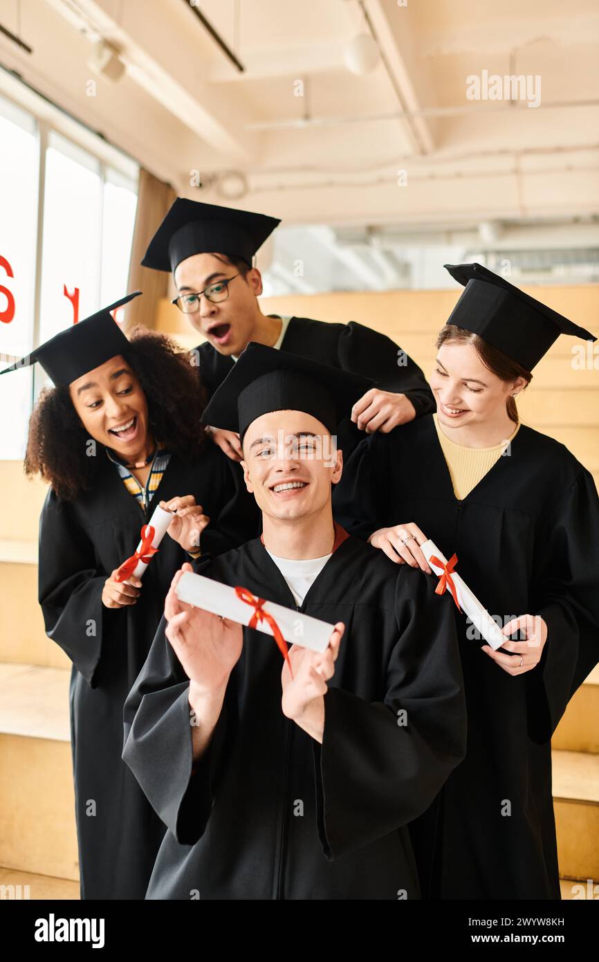 Eine vielfältige Gruppe von Studenten in Abschlusskleidern und akademischen Mützen posiert glücklich für ein Foto drinnen. Stockfoto