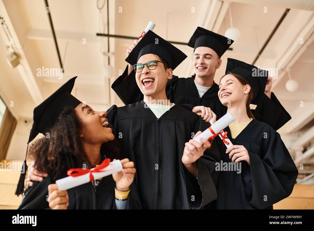 Gruppe freudiger Studenten in Abschlussmützen und -Kleidern, die ihre akademischen Leistungen bei einer Universitätszeremonie feiern. Stockfoto