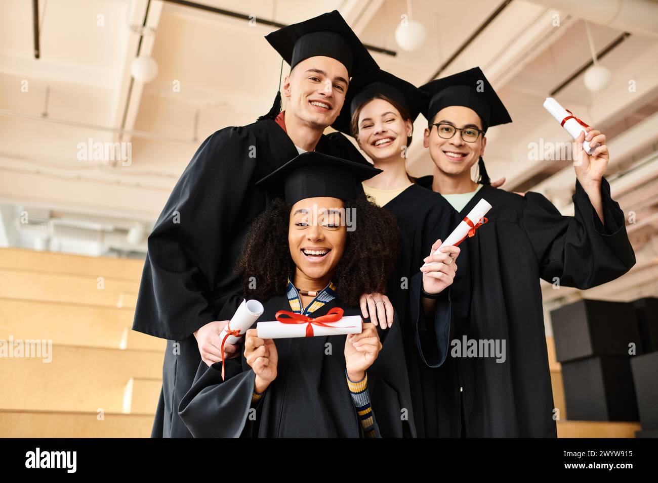 Verschiedene Gruppen von Studenten in Abschlusskleidern und akademischen Mützen lächeln glücklich für ein Foto drinnen. Stockfoto