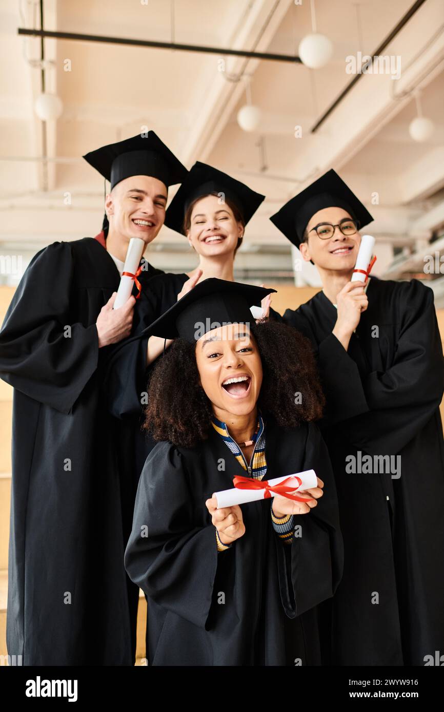 Eine bunte Gruppe glücklicher Studenten in Abschlusskleidern posiert für ein Foto drinnen. Stockfoto