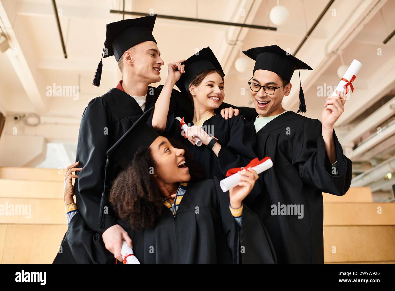 Eine vielfältige Gruppe glücklicher Studenten in Abschlusskleidern und akademischen Mützen posiert für ein Foto drinnen. Stockfoto
