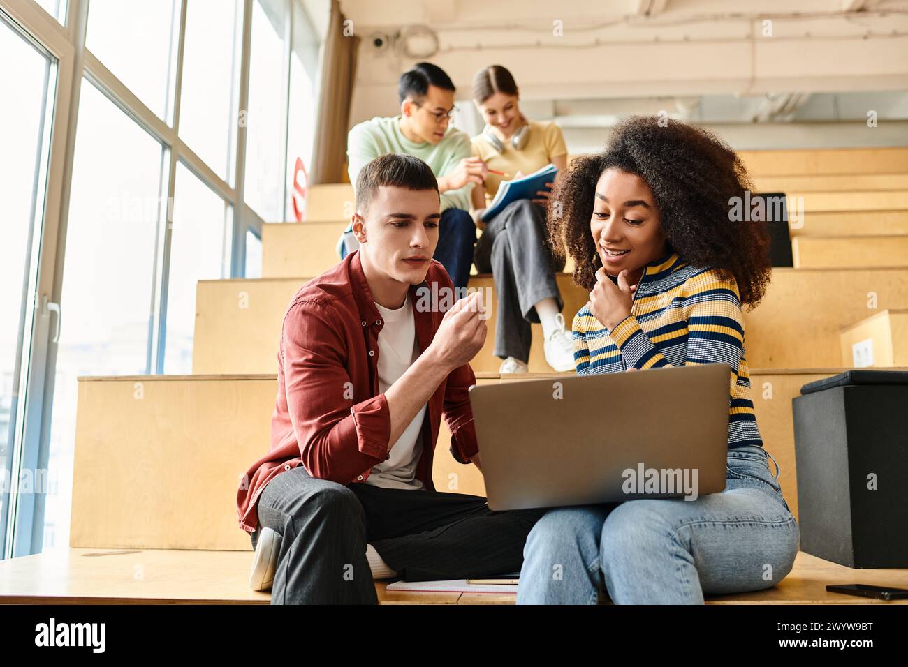 Multikulturelle Gruppe junger Studenten, die auf den Stufen eines Gebäudes sitzen und sich auf den Laptop-Bildschirm konzentrieren Stockfoto