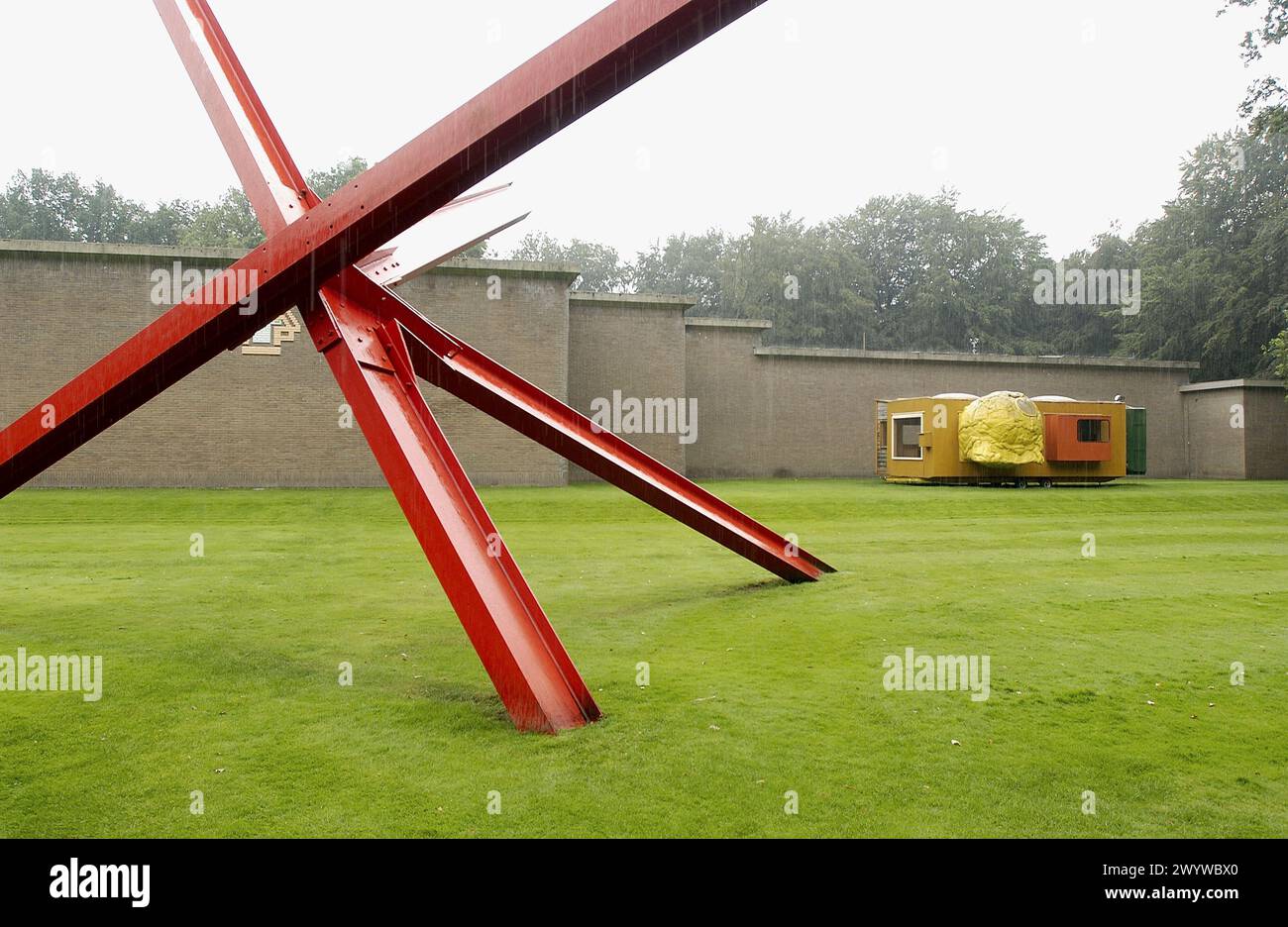 K-Stück von Mark di Suvero und Mobile Home von Joep Van Lieshout im Hintergrund, Kröller-Müller Museumgarten, Het nationale Park de Hoge Veluwe. Gelderland, Niederlande. Stockfoto