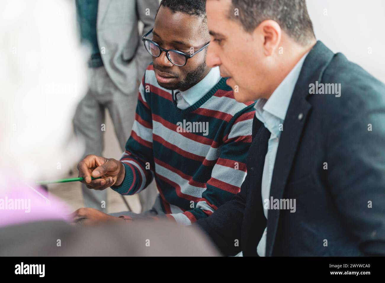 Ein konzentriertes Paar von Fachleuten, ein afrikanischer Mann und ein kaukasischer Mann, untersuchen Dokumente genau, diskutieren Strategien in einem Team-Meeting, ihre Stockfoto
