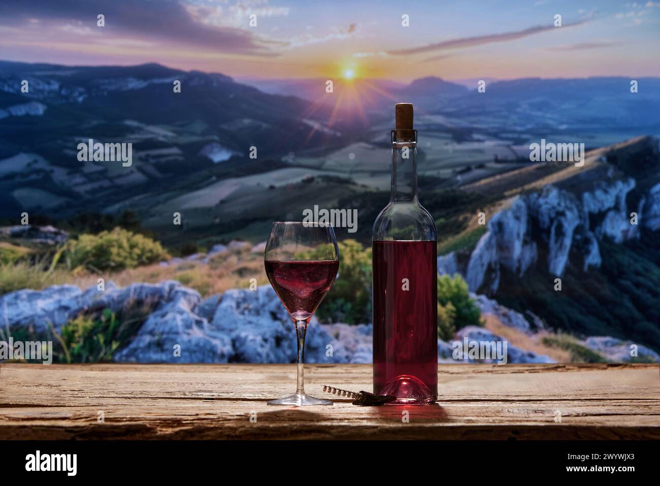 Flasche Rotwein und Glas auf Holztisch im Freien. Berg und Ablage während der Abendzeit im Hintergrund. Stockfoto