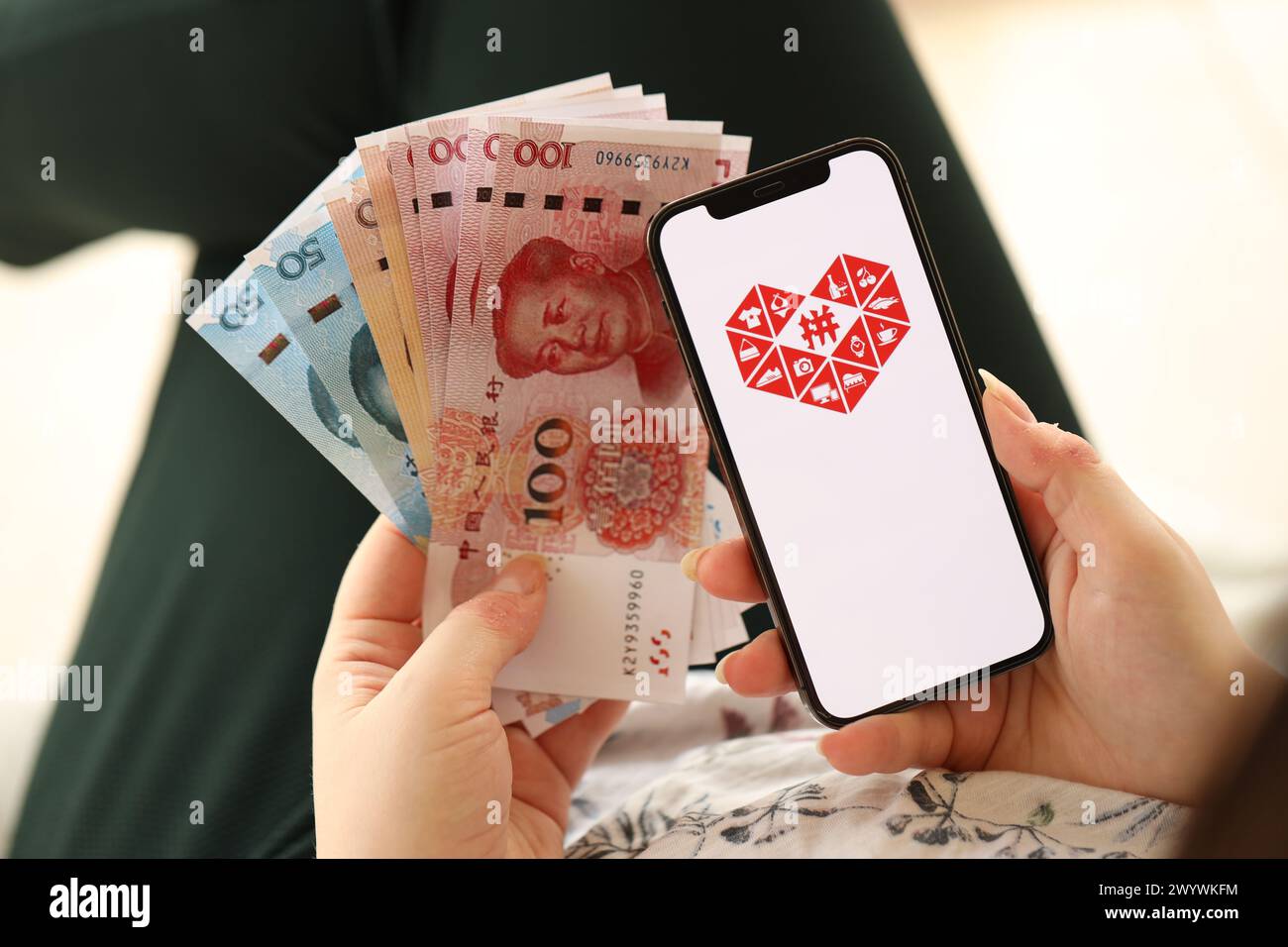 KIEW, UKRAINE - 1. APRIL 2024 Pinduoduo-Symbol auf dem Smartphone-Bildschirm und Geld in weiblicher Hand. IPhone-Display mit App-Logo und chinesischen Yuan-Geldscheine in Frauenhänden aus nächster Nähe Stockfoto