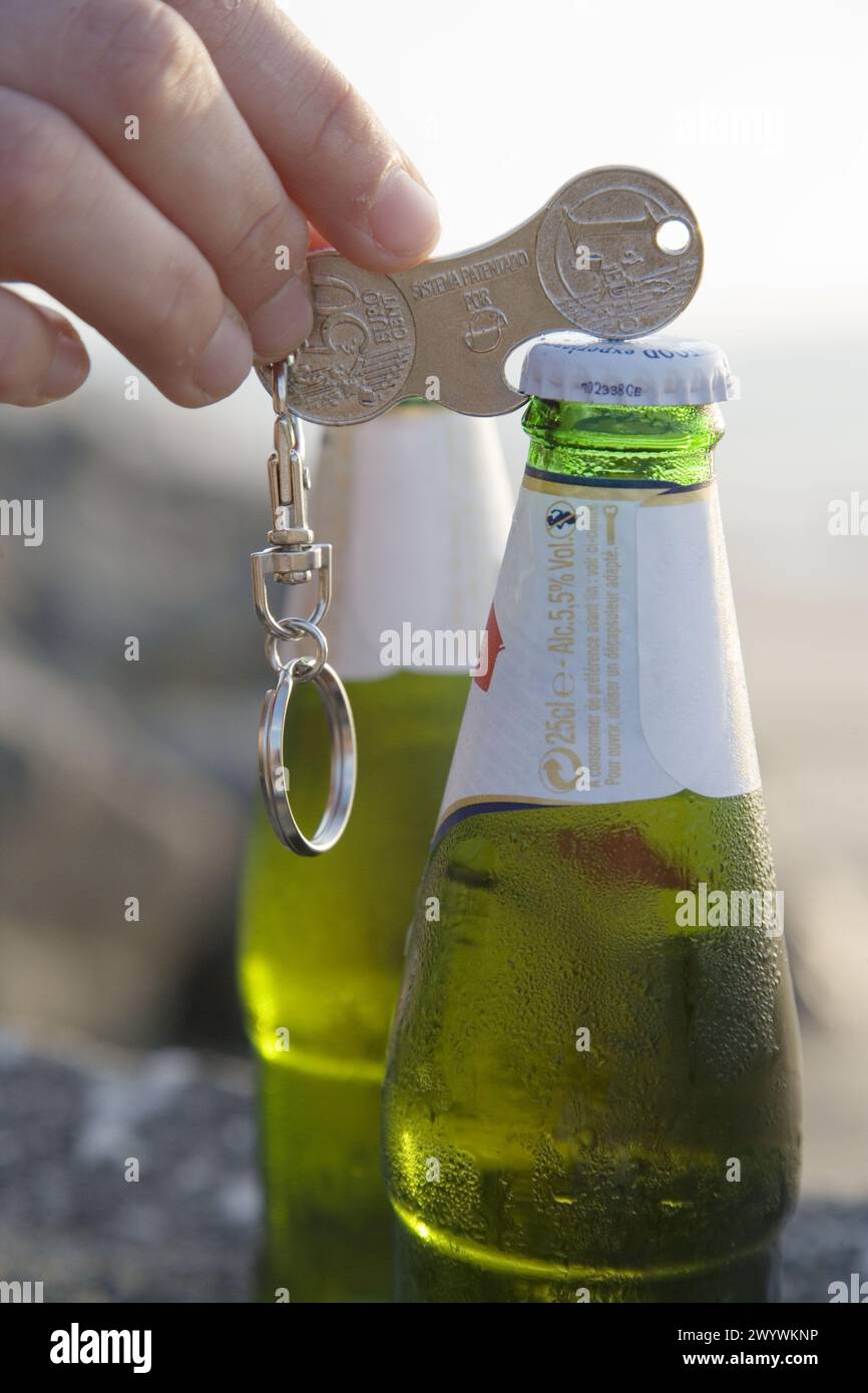 Öffnen der Bierflasche mit einem münzförmigen Schlüsselanhänger. Stockfoto