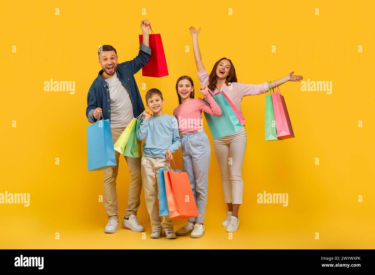 Familie feiert Einkaufserfolg auf gelbem Hintergrund Stockfoto