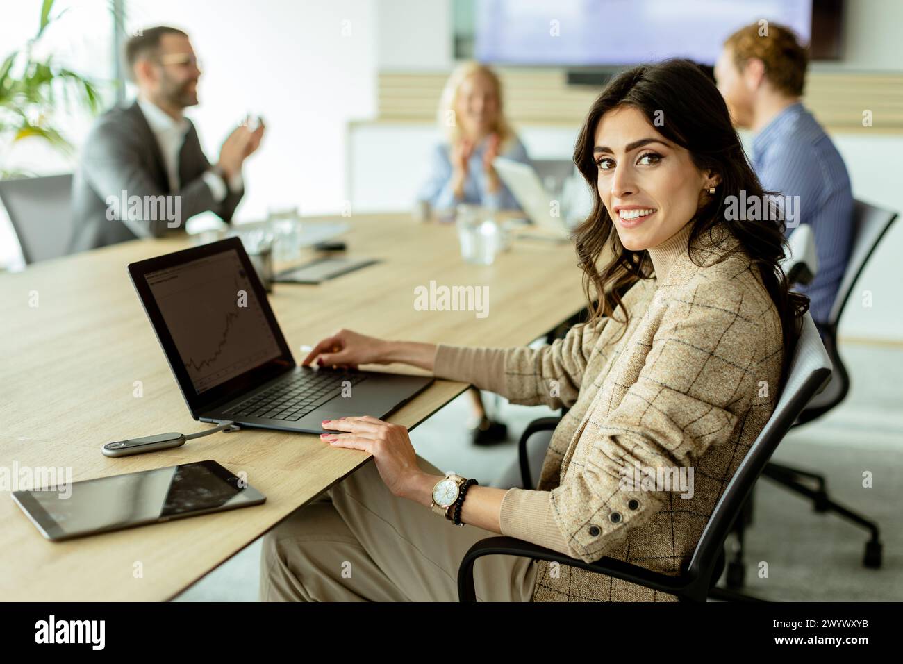 Selbstbewusste Geschäftsfrau engagiert sich in einem Meeting, ihr Lächeln spiegelt Erfolg und Teamarbeit in einem modernen Büroumfeld wider. Stockfoto