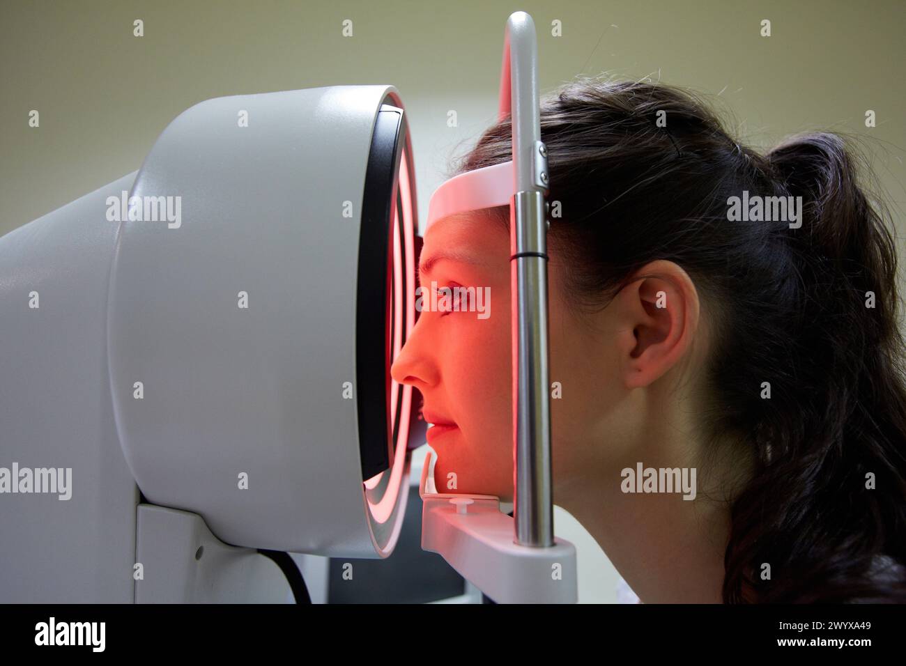 Augenuntersuchung Patient mit einer Hornhauttopographie, die am Auge gemessen wird. Das Gerät in der Mitte projiziert helle Ringe auf das Auge, die durch Untersuchung der Reflexion in seiner Oberfläche reflektiert werden. die Hornhaut ist der vordere Teil des Auges, der Iris und Pupille bedeckt. Sie ist für den Großteil der Lichtfokussierung verantwortlich. da nur eine feine Fokussierung durch die Linsendefekte in Form der Hornhaut zu einer Vielzahl von Fokussierungsstörungen führen kann, können diese operativ oder durch das Tragen von maßgeschneiderten Kontaktlinsen oder spect behandelt werden Stockfoto
