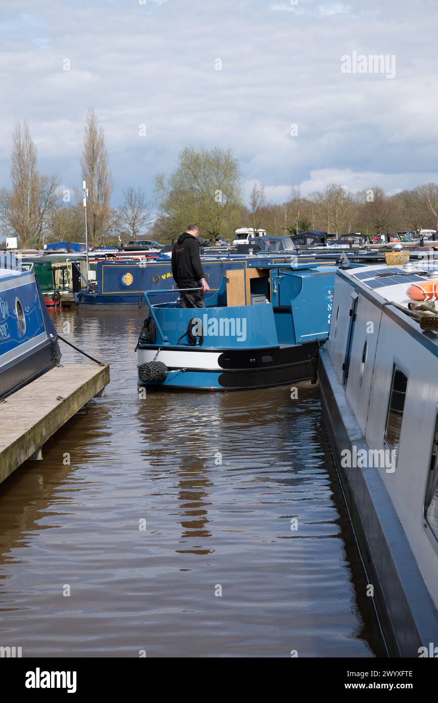 Mann an der Tilger eines neuen Schmalbootes, der vorsichtig in einen Ponton fährt, der in einem Yachthafen im Binnenschiffsverkehr am Shropshire Union Canal ankert. Stockfoto