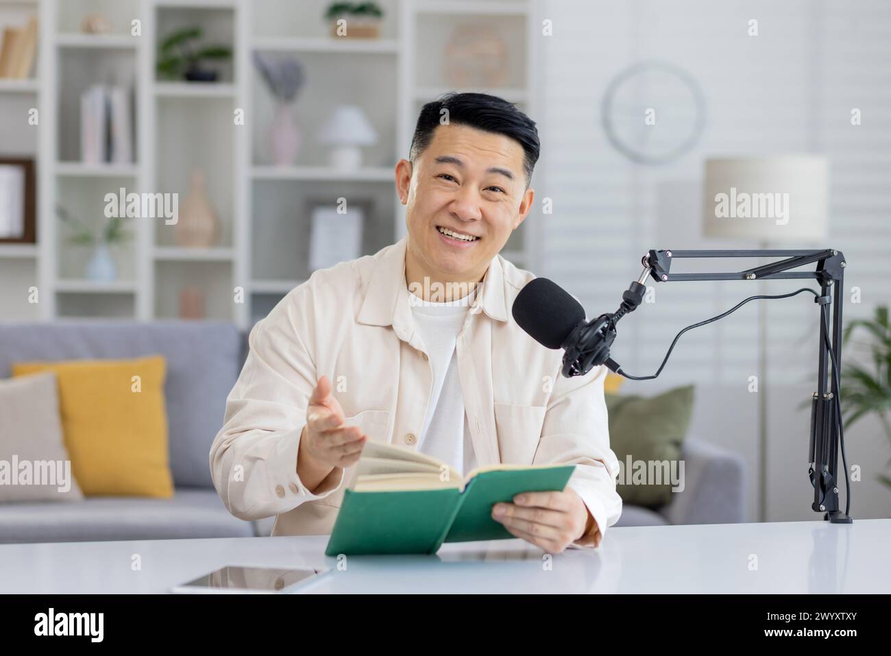 Eine fokussierte Person, die eine virtuelle Buchlesung mit Mikrofon und Buch in einer häuslichen Umgebung durchführt. Stockfoto