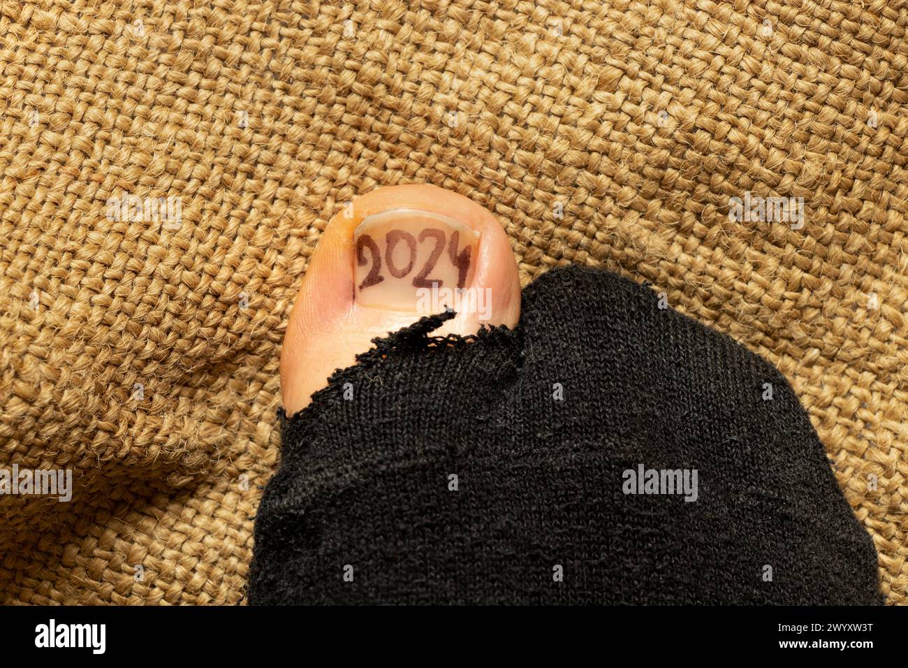 2024 wird auf einem Mädchenzehe gezeichnet, der aus einer gerissenen Socke, Armut und Misserfolg ragt Stockfoto