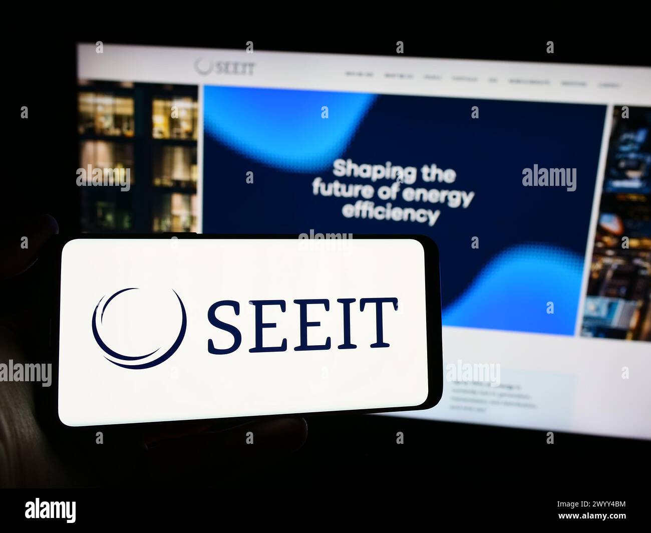 Person mit Mobiltelefon und Logo des Unternehmens SDCL Energy Efficiency Income Trust (SEEIT) vor der Webseite. Schwerpunkt auf dem Display des Telefons. Stockfoto