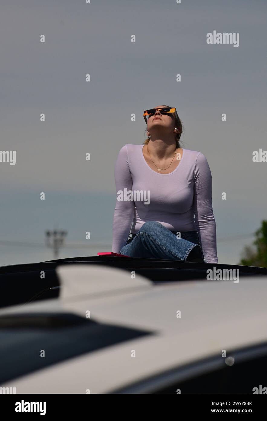 Mt. Vernon, USA. April 2024. Molly Miller aus Chicago sitzt auf dem Dach eines Autos, um die Sonnenfinsternis auf dem Walmart-Parkplatz in Mt. Vernon, IL - in der Nähe des Zentrums des Pfades der Totalität - Montag, 8. April 2024. Sie hatte Geschäfte in St. Louis, und anstatt zu fliegen, wie sie es normalerweise tut, fuhr sie, damit sie einen Tag früher ankommen konnte, um die Sonnenfinsternis zu sehen. Foto: Tim Vizer/SIPA USA Credit: SIPA USA/Alamy Live News Stockfoto