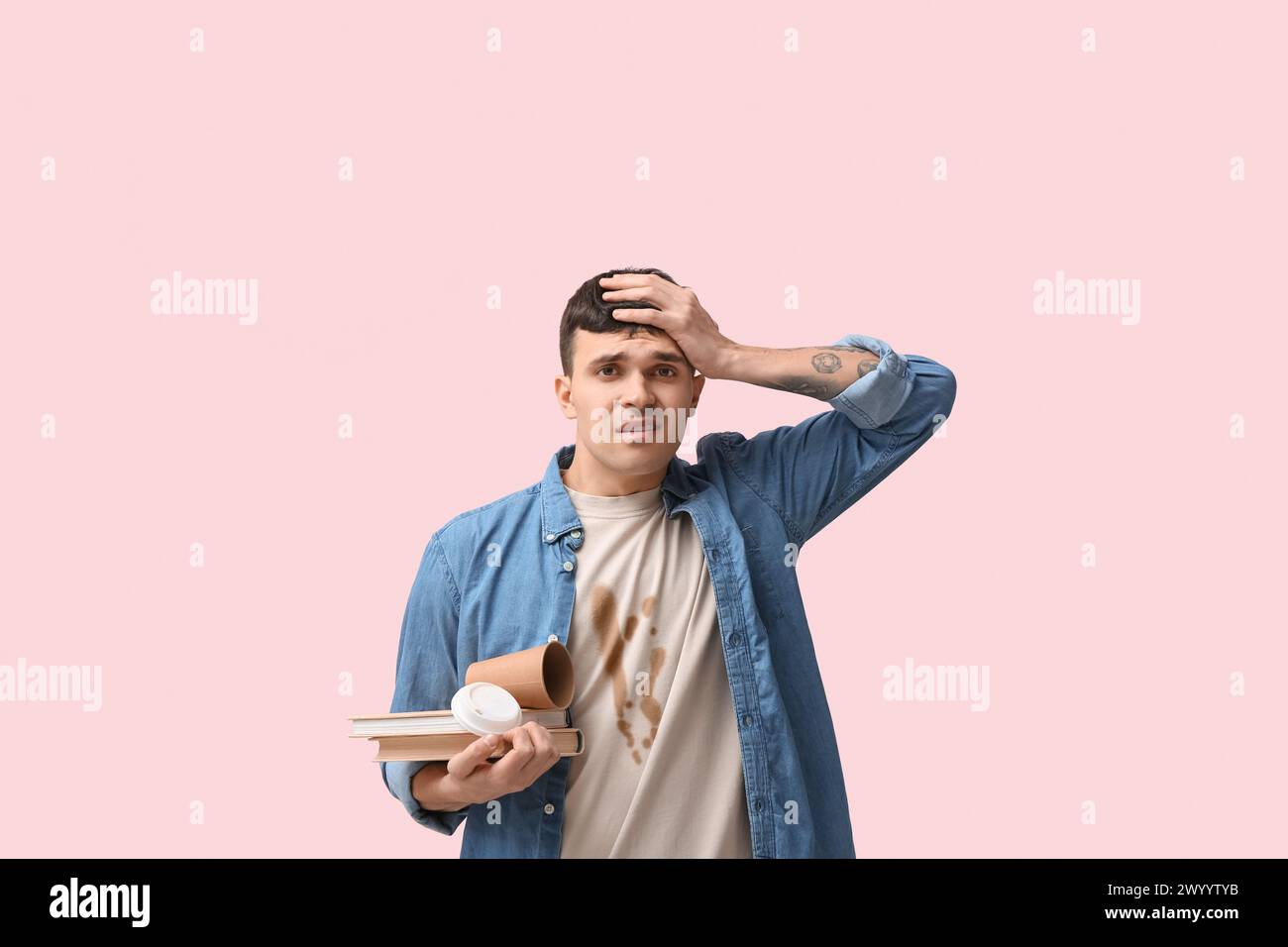 Gestresster Schüler in schmutzigem T-Shirt mit Büchern und Pappbecher auf rosa Hintergrund Stockfoto