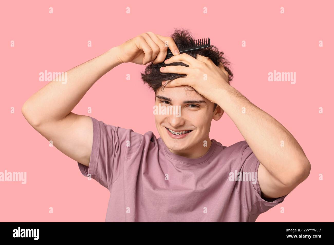 Junger Mann, der Haare auf rosa Hintergrund kämmt Stockfoto