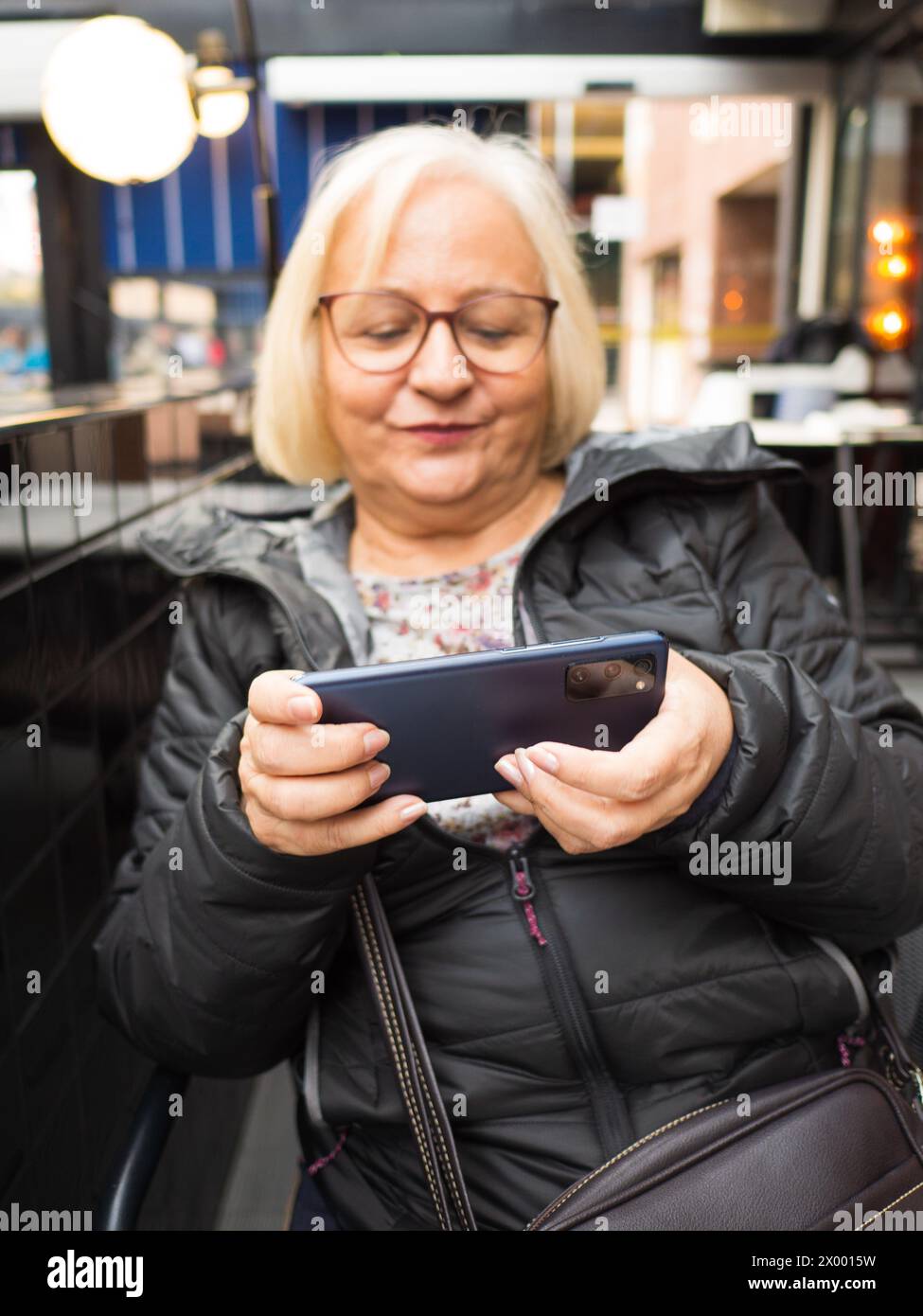 Unfokussierte blonde Gamer Großmutter hat sich sehr auf das Smartphone konzentriert Stockfoto