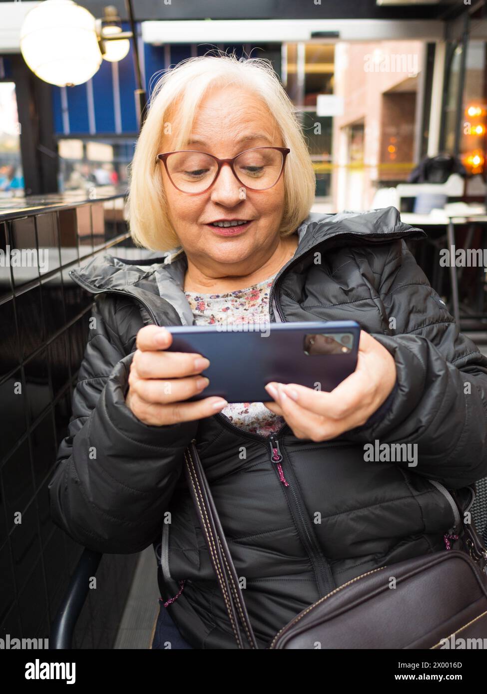 Die blonde Gamer Großmutter ist überrascht, auf dem Smartphone zu spielen Stockfoto
