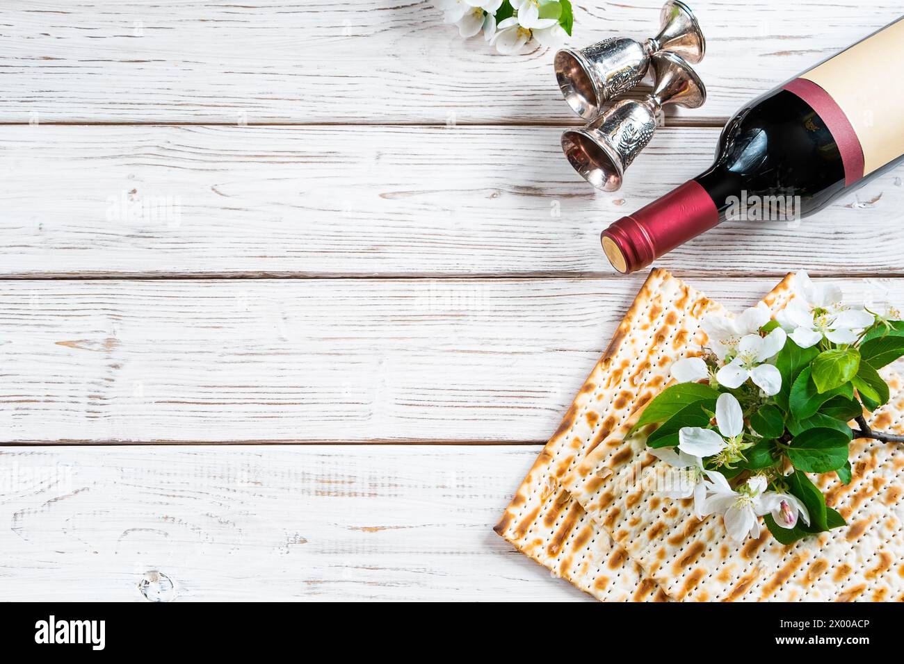 Wir feiern den jüdischen Pessach-Feiertag. Flasche Wein, Matzo und Blumen auf weißem Holzhintergrund. Festliches Flatlay. Kopierbereich. Stockfoto