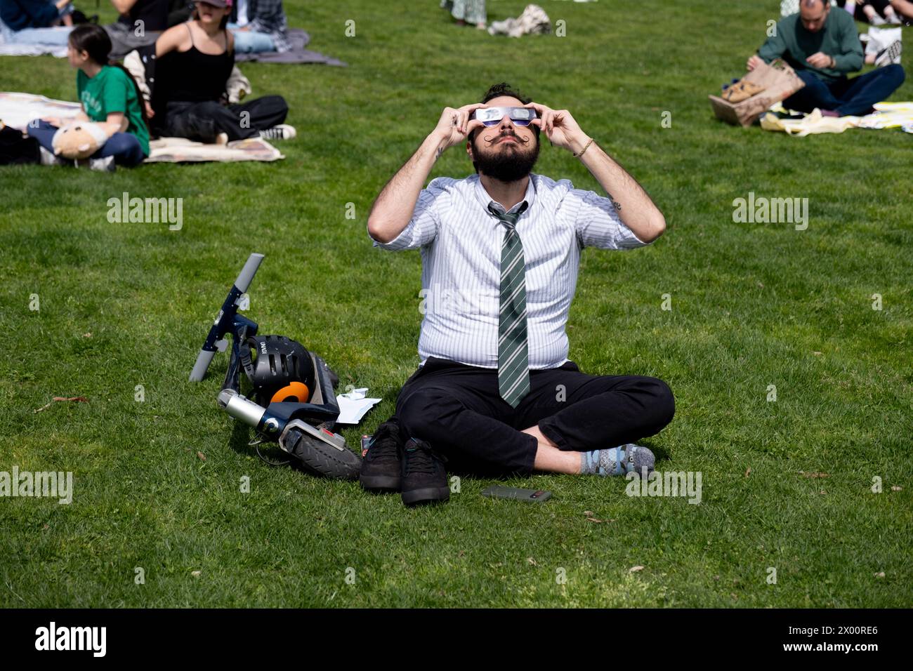 New York, Usa. April 2024. Ein Mann mit einem Schnurrbart sieht durch seine Sonnenfinsternis-Brille, während er auf dem Gras sitzt. New Yorker versammelten sich im Central Park, um die Sonnenfinsternis zu sehen. Die Sonne wurde vom Mond um 90 % verdeckt, nur schüchtern vor der Totalität. Die letzte Sonnenfinsternis in New York City war 2017 und erreichte 70 %. Die nächste Sonnenfinsternis für die Stadt wird im Jahr 2045 mit nur 50 % sein. Die New Yorker müssen bis Mai 2079 warten. (Foto: Syndi Pilar/SOPA Images/SIPA USA) Credit: SIPA USA/Alamy Live News Stockfoto