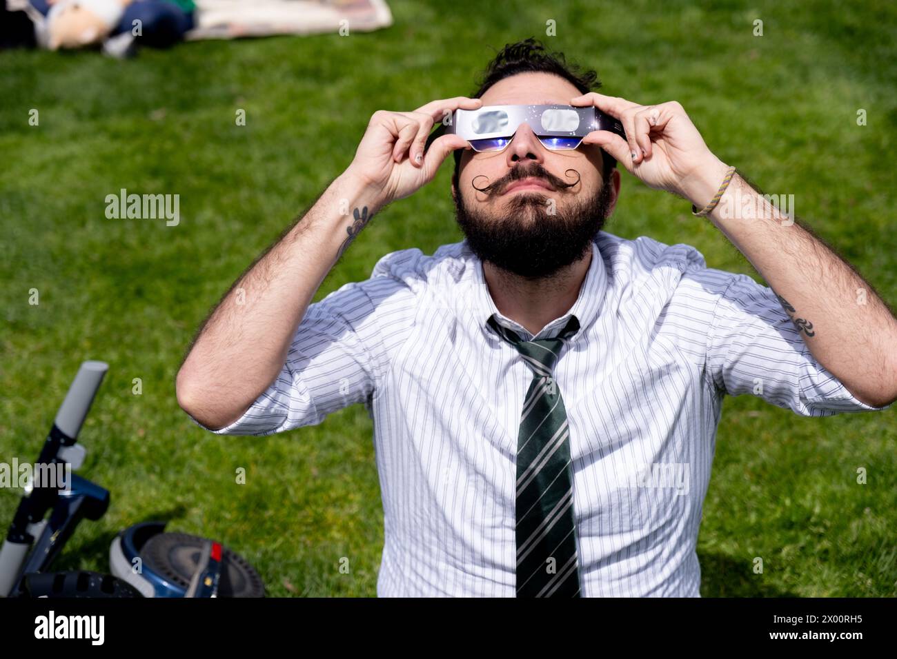 New York, Usa. April 2024. Ein Mann mit einem Schnurrbart sieht durch seine Sonnenfinsternis-Brille, während er auf dem Gras sitzt. New Yorker versammelten sich im Central Park, um die Sonnenfinsternis zu sehen. Die Sonne wurde vom Mond um 90 % verdeckt, nur schüchtern vor der Totalität. Die letzte Sonnenfinsternis in New York City war 2017 und erreichte 70 %. Die nächste Sonnenfinsternis für die Stadt wird im Jahr 2045 mit nur 50 % sein. Die New Yorker müssen bis Mai 2079 warten. Quelle: SOPA Images Limited/Alamy Live News Stockfoto