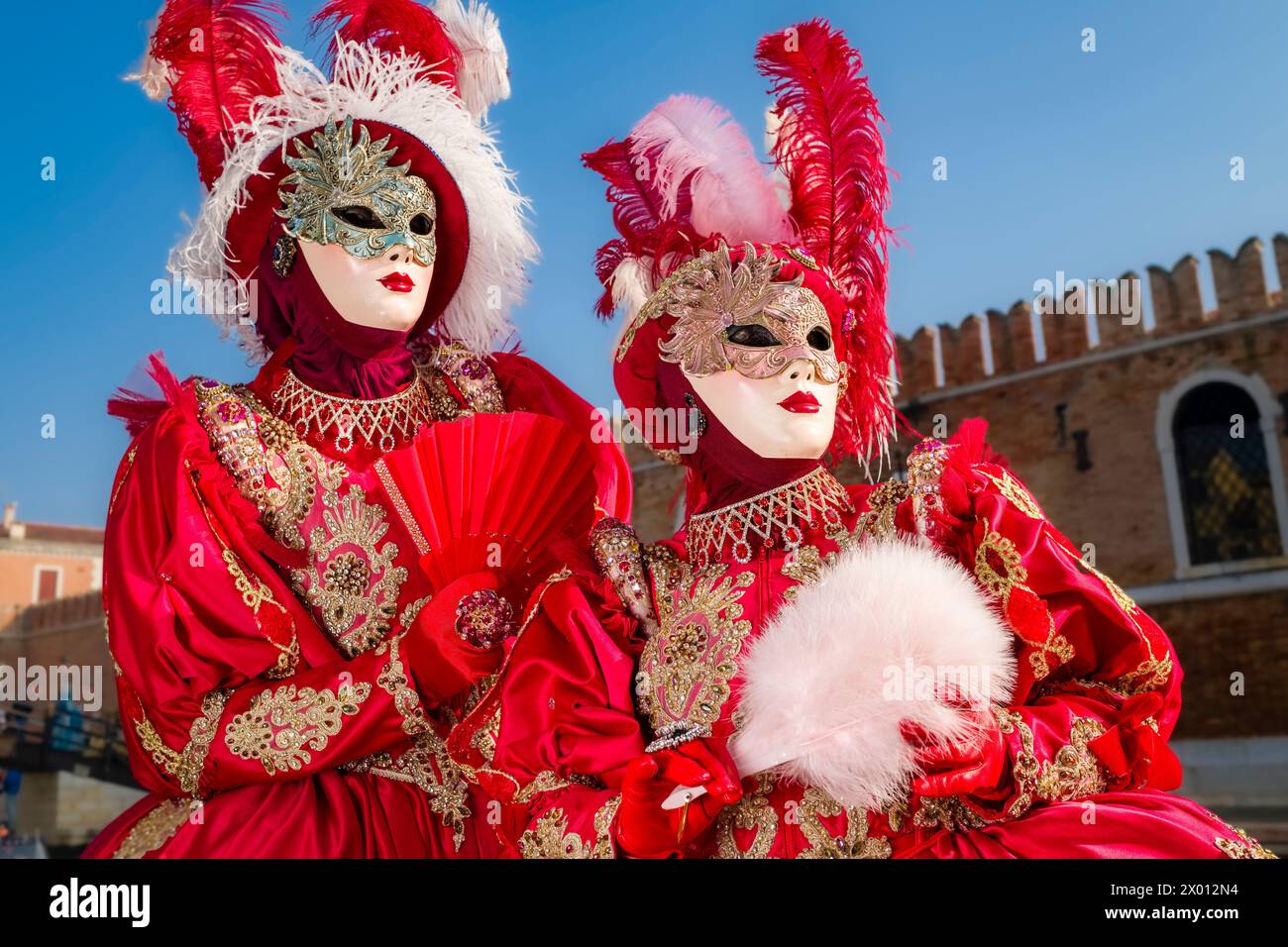 Porträts von zwei weiblichen maskierten Personen in kreativen Kostümen, die in den Gebäuden von Arsenale posieren, um den venezianischen Karneval zu feiern. Stockfoto