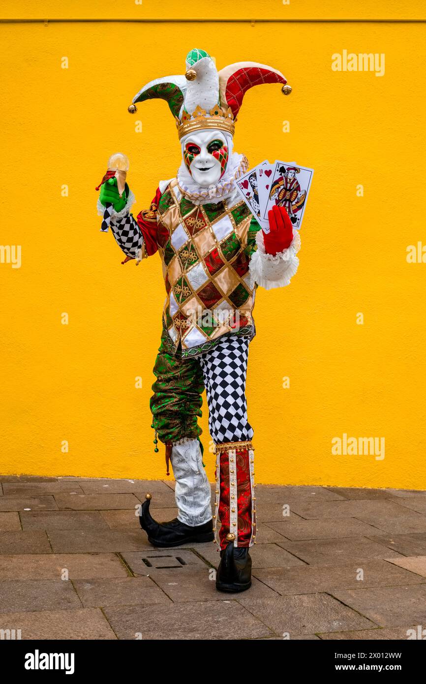 Eine maskierte Person in einem kreativen Harlekin-Kostüm, posiert vor einer gelben Wand auf der Insel Burano, um den venezianischen Karneval zu feiern. Stockfoto