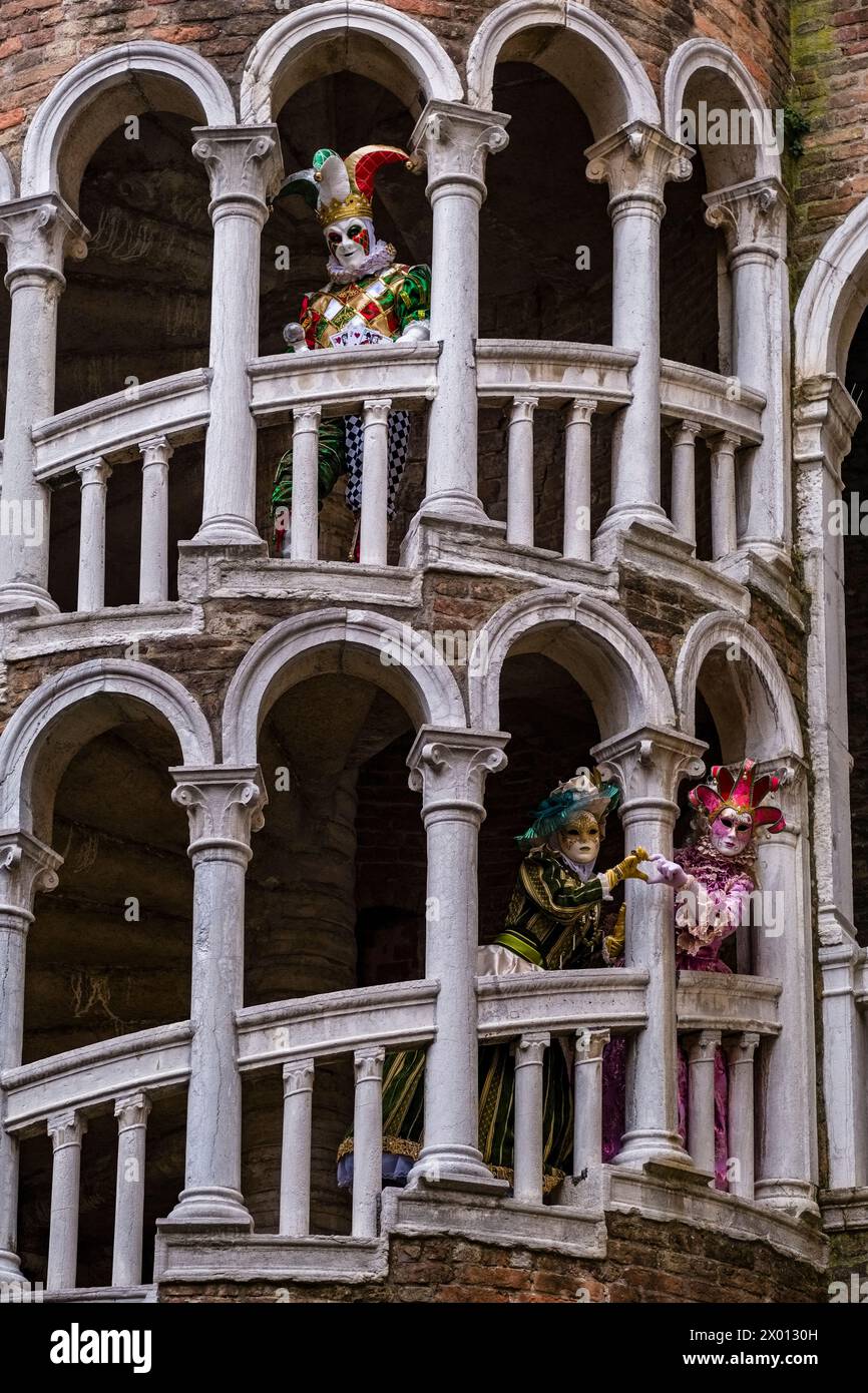 Einige maskierte Personen in kreativen Kostümen posieren auf der Treppe der Scala Contarini del Bovolo, um den venezianischen Karneval zu feiern. Stockfoto