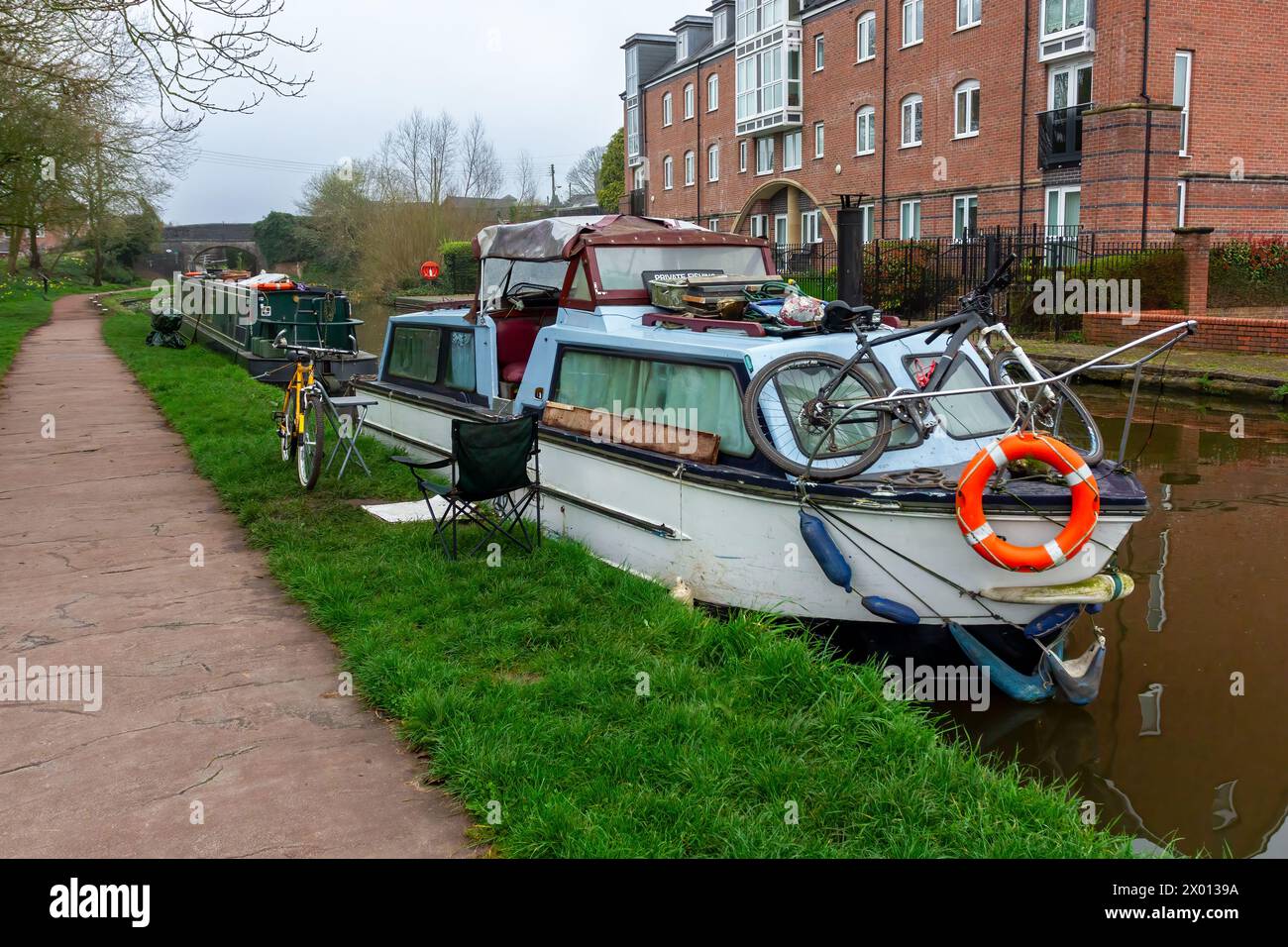 Ein Kanalboot liegt am Schleppweg. Fahrräder stehen draußen. Einer liegt auf dem Gras, der andere auf der Vorderseite des Bootes. Stockfoto