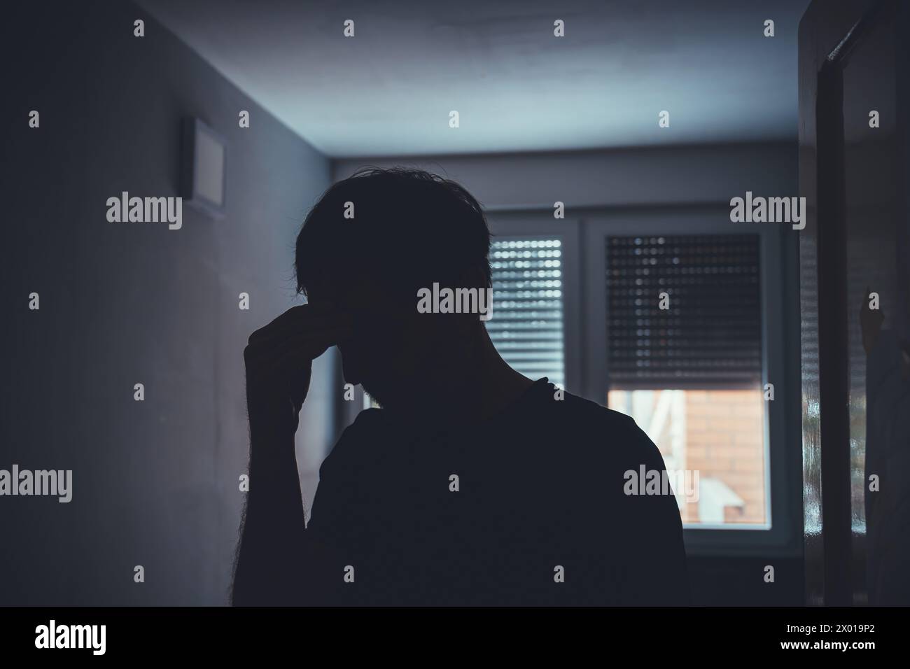Silhouette eines depressiven traurigen Mannes in einem dunklen Raum mit heruntergezogenen Fensterläden, selektiver Fokus Stockfoto