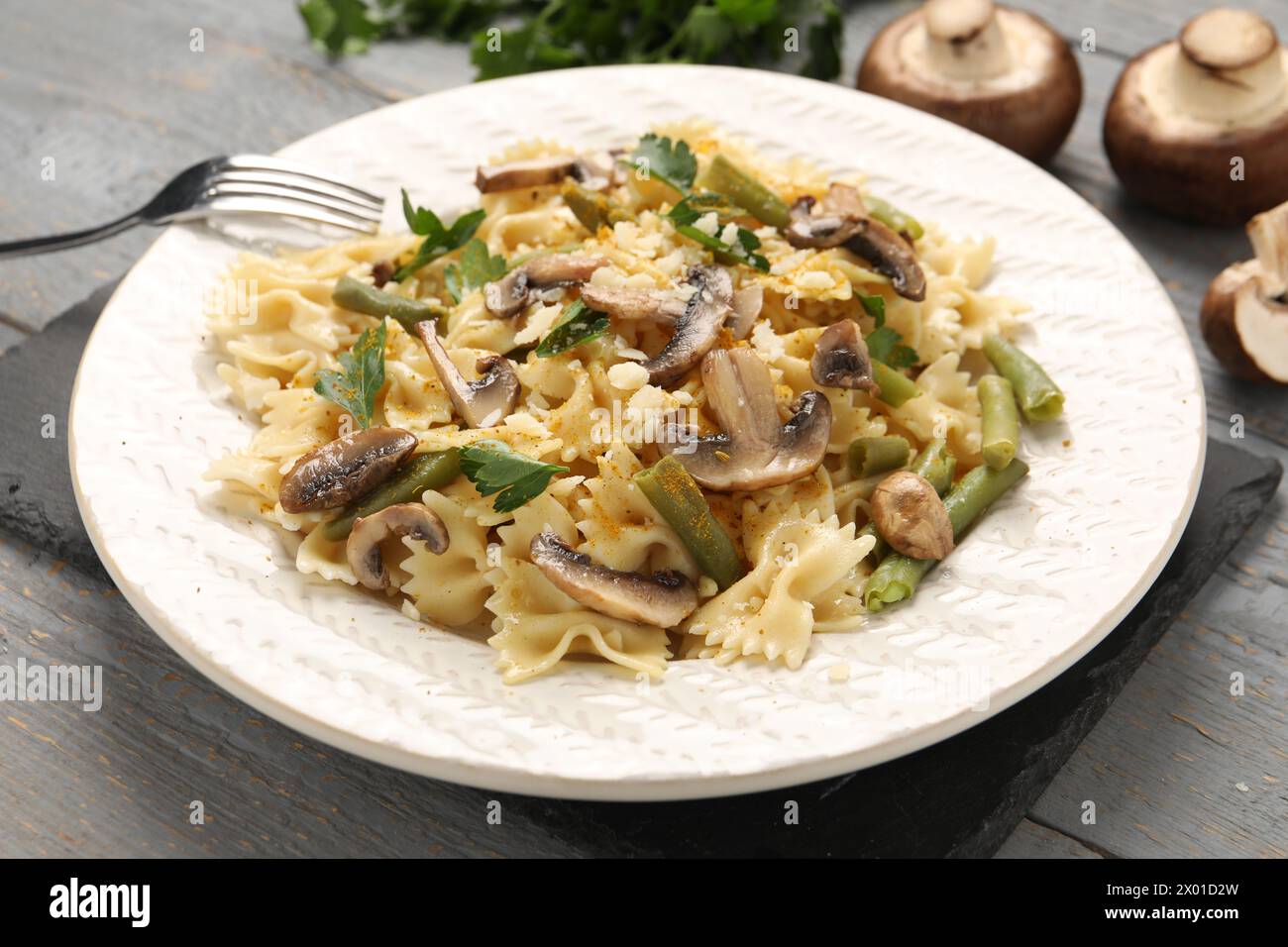 Vegetarische Pasta mit Pilzen, Petersilie, Bohnen und Käse auf grauem Holztisch, Nahaufnahme Stockfoto