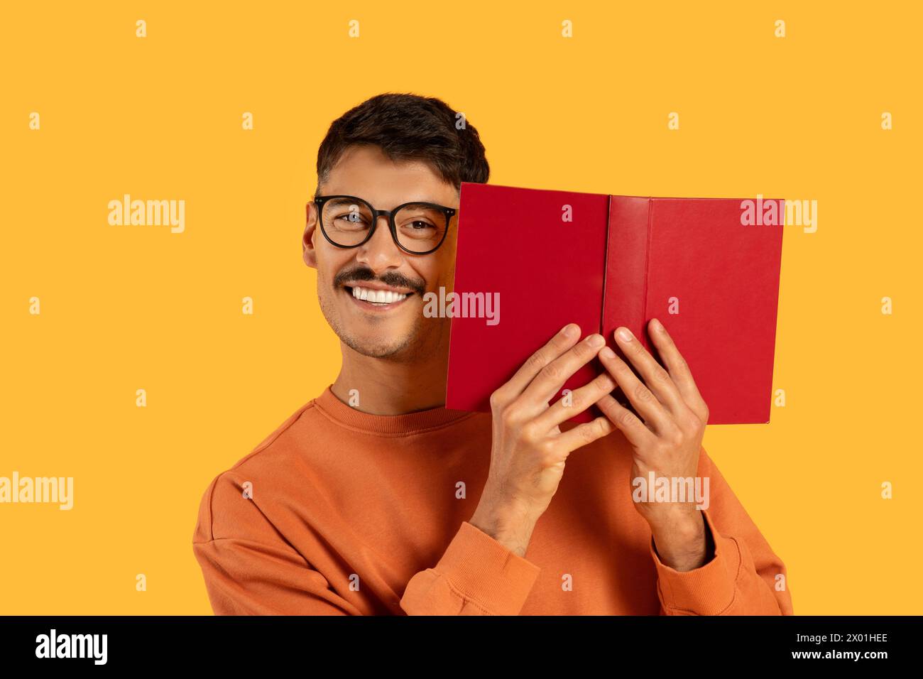 Mann, der sein Gesicht mit Buch bedeckt und lächelt Stockfoto