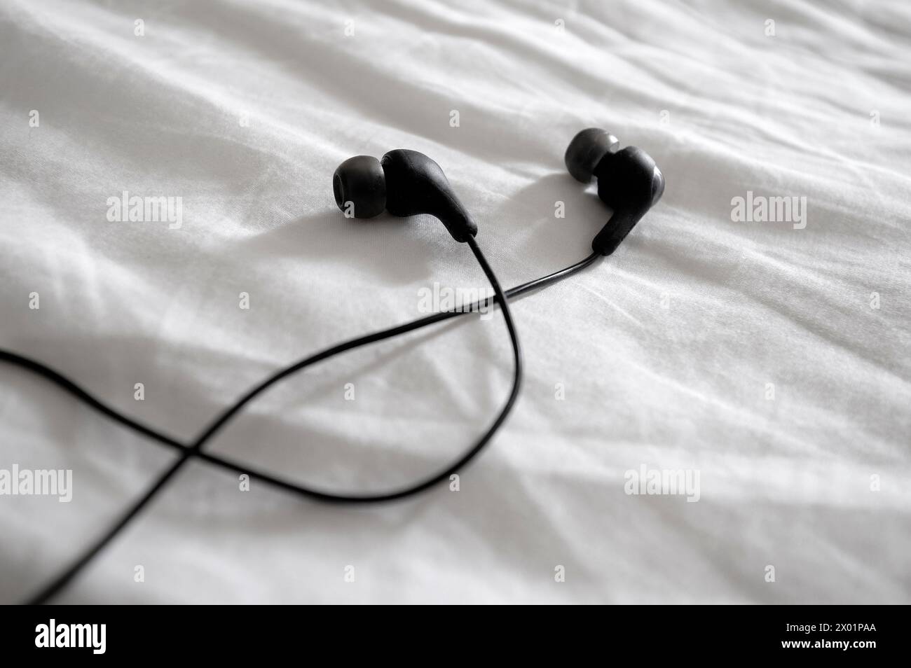 Ohrhörer auf weißem, gefaltetem Bettlaken Stockfoto