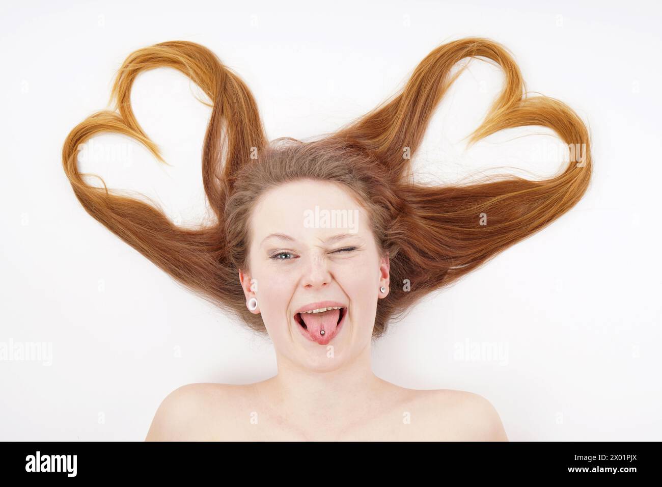 Junge Frau, deren Haare Herzform bilden und zwinkern, während sie die Zunge herausstechen Stockfoto