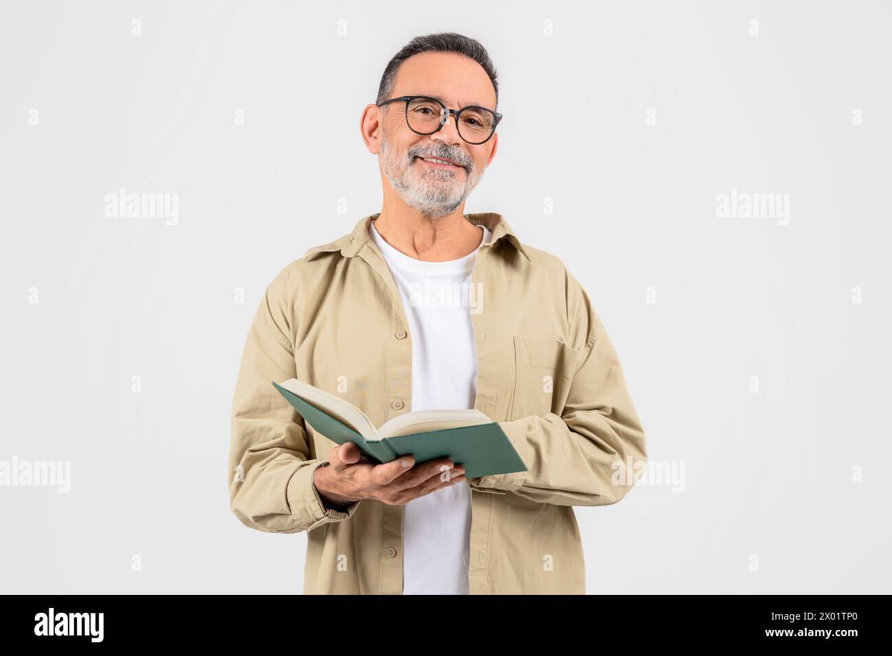 Ein Mann liest aufmerksam ein grünes Buch auf weißem Hintergrund Stockfoto