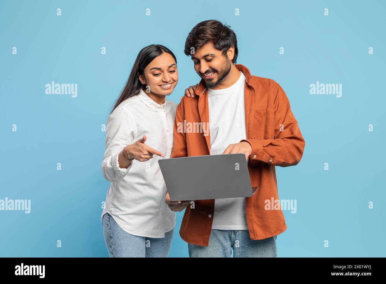 Verlobtes Paar, das auf einen Laptop auf blauem Hintergrund blickt Stockfoto