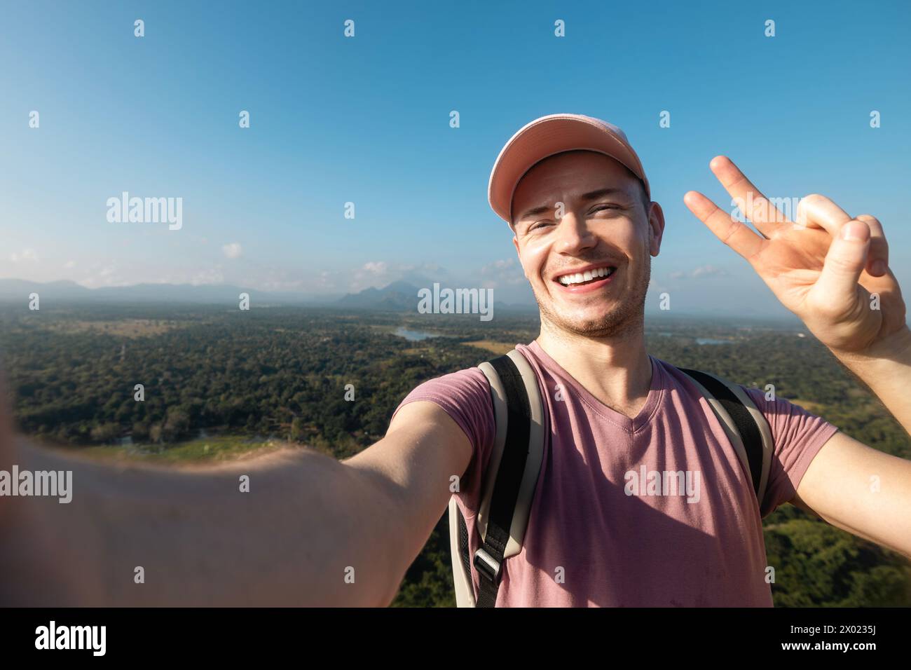 Glücklicher Mann, der Selfie vom Sommerferientag macht. Hübscher Tourist mit Mütze und einem Lächeln vor der Kamera vor tropischer Landschaft. Stockfoto