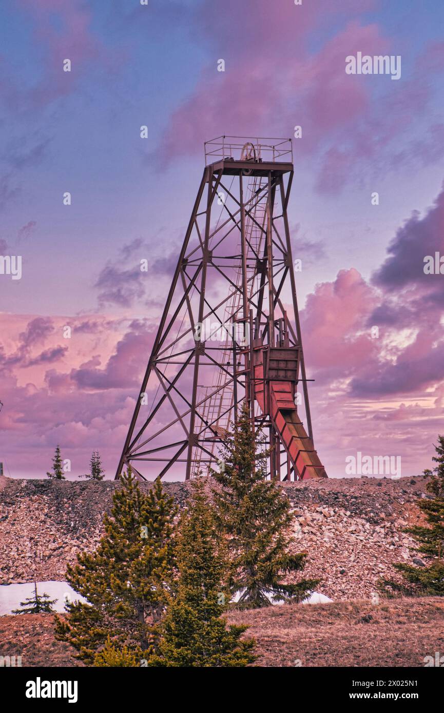Ein hoch aufragendes altes Bergbauwerk inmitten von Pinienbäumen unter einem atemberaubenden Himmel bei Sonnenuntergang, das die Überreste von Colorados Herzland und seine reiche Geschichte zeigt Stockfoto