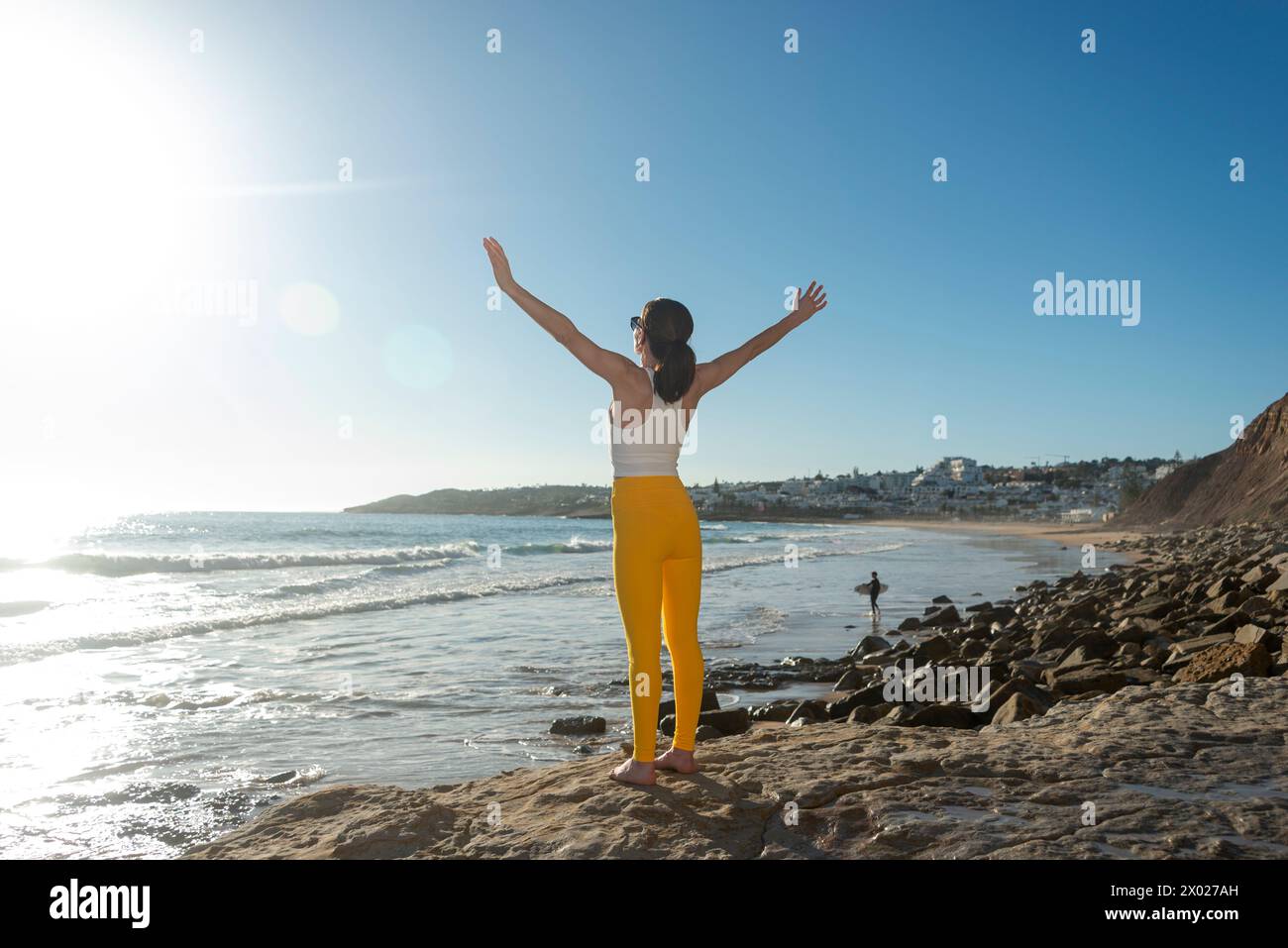 Sportliche Frau, die mit erhobenen Armen am Meer steht und die Sonne genießt, positive Emotionen Stockfoto