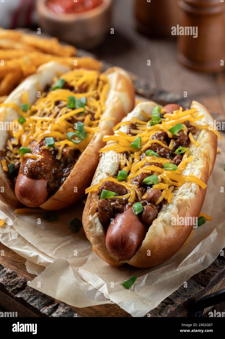 Zwei Chili Hot Dogs mit geriebenem Cheddar und gehackten grünen Zwiebeln auf Holztablett Stockfoto