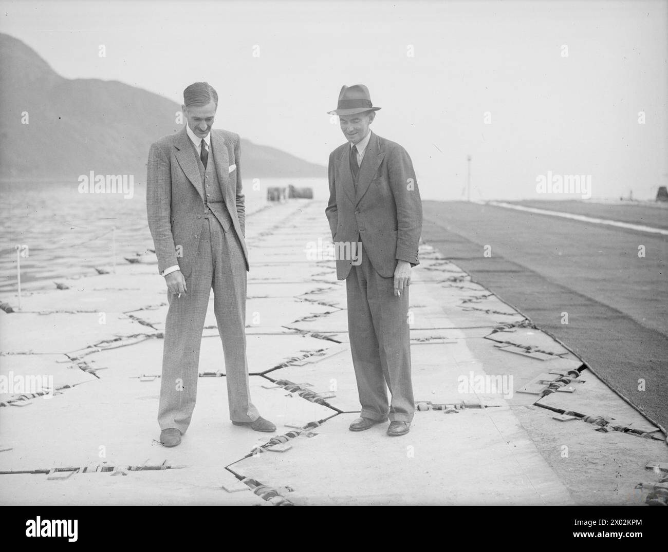 FLUGPLATZ „THE LILY“. 30. AUGUST 1945, LAMLASH SCOTLAND. WÄHREND DER TESTS MIT DEM EXPERIMENTELLEN LUFTSTREIFEN „LILY“, DER SCHWIMMENDEN „INSEL“, DIE VON MR. R M HAMILTON ERFUNDEN WURDE UND AUS SECHSECKIGEN AUFTRIEBSTROMMELN BESTEHT, DIE ZUSAMMENKLAPPBAR SIND, UM EINE FLEXIBLE LANDEFLÄCHE FÜR FLUGZEUGE AUF SEE ZU BILDEN. ER IST 520 FT LANG UND 60 FT QUER. - Mr. R M Hamilton und Mr. J S Herbert fotografierten auf "Lily". Die Art und Weise, wie die sechseckigen Trommeln geschwenkt werden, ist im Bild zu sehen Stockfoto