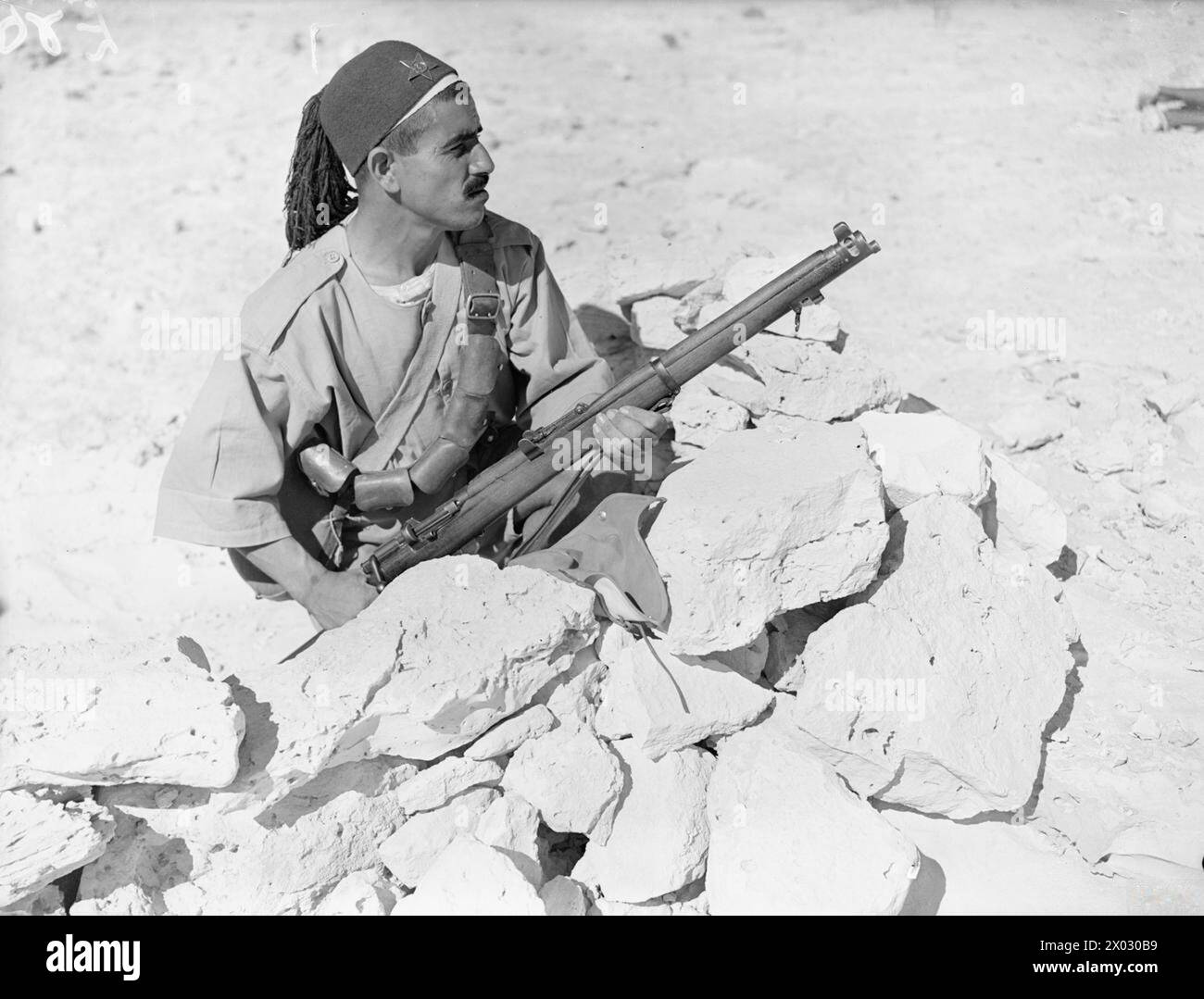 DIE ARABISCHE LEGION IN NORDAFRIKA - ein Schützling der Arabischen Legion, bewaffnet mit einem SMLE (Short Magazine Lee-Enfield) Mk III, Schutz hinter Felsen, Mersa Matruh, Ägypten, 28. Mai 1940 Arabische Legion Stockfoto