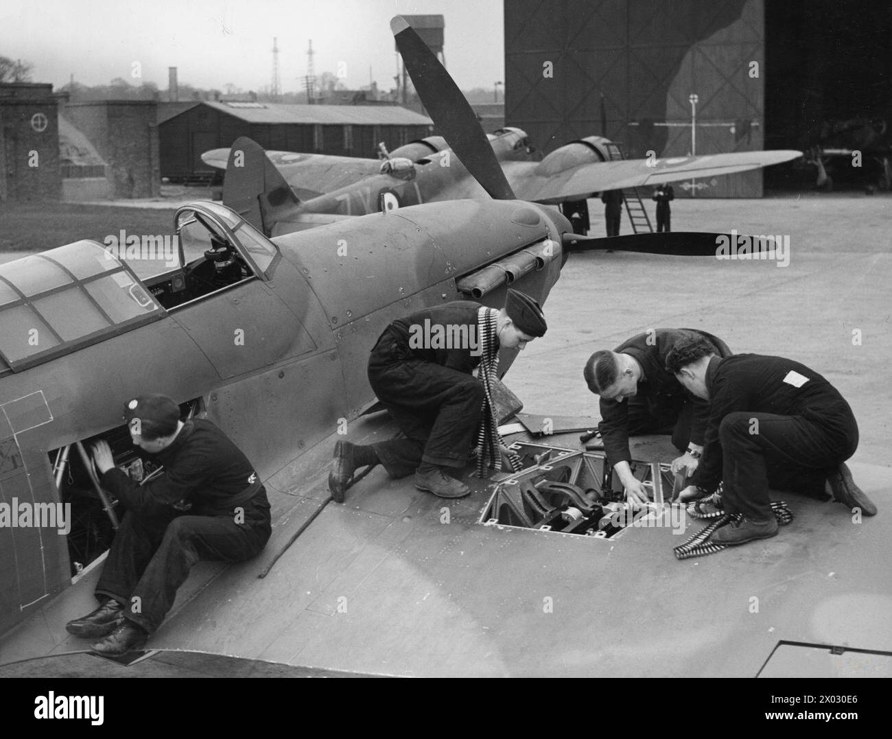 RAF-JAGDKOMMANDO IM ZWEITEN WELTKRIEG – Ein neu ausgelieferter Hawker Hurrikan Mk I wurde im April 1940 auf einem RAF-Flugplatz in Großbritannien, wahrscheinlich North Weald, bewaffnet. Im Hintergrund ist ein Blenheim Mk IF der Nr. 25 Geschwader zu sehen Stockfoto