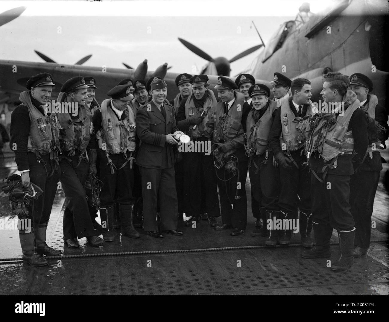 ANGRIFF AUF FEINDLICHE SCHIFFE VOR NORWEGEN. 26. NOVEMBER 1944 AN BORD DES LUFTFAHRZEUGTRÄGERS HMS INPLACABLE. DIE FLOTTENPILOTEN UND DIE BESATZUNG, DIE AM ERFOLGREICHEN ANGRIFF AUF DIE FEINDLICHE SCHIFFFAHRT VOR DER KÜSTE NORWEGENS TEILNAHMEN. - Einige der Männer, die an den Angriffen teilnahmen, fotografiert mit Captain W F Kline, USN, dem US Naval Air Attache, der eine Holzaschenschale aus UNERBITTLICHEM Holz hält und ihm vom Schiff präsentiert wird Stockfoto